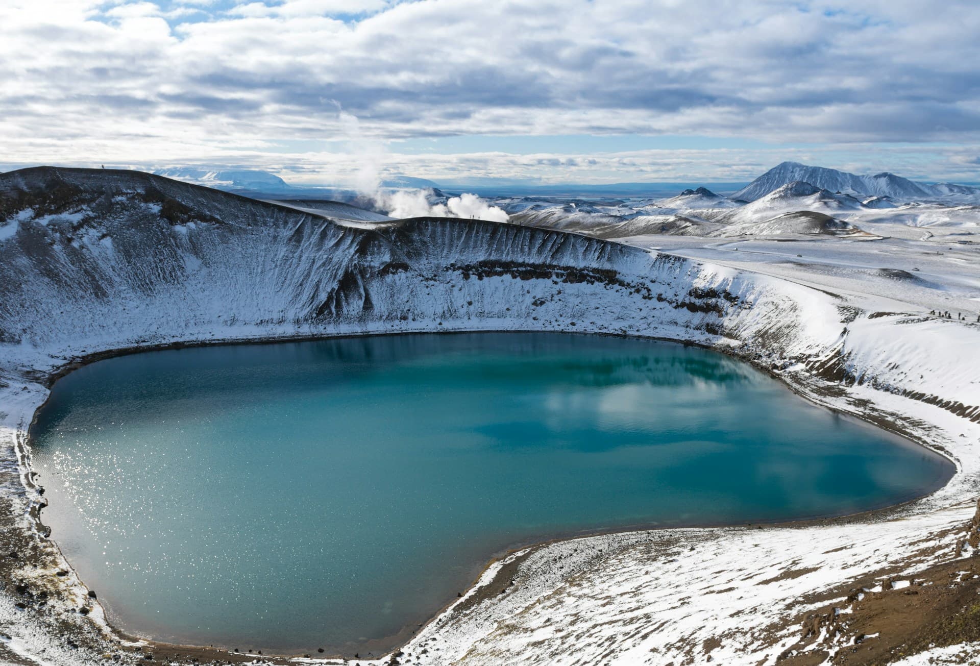 Turquoise volcanic crater lake ringed by snow in North Iceland
