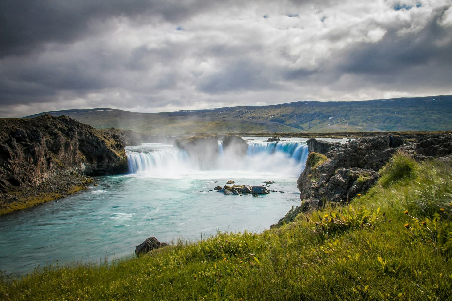 Goðafoss waterfall cascading into a turquoise river under cloudy skies