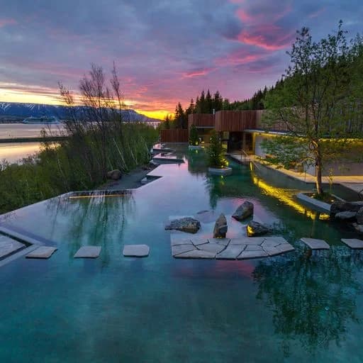 Infinity-edge geothermal pool with stone pathways overlooking a fjord at sunset