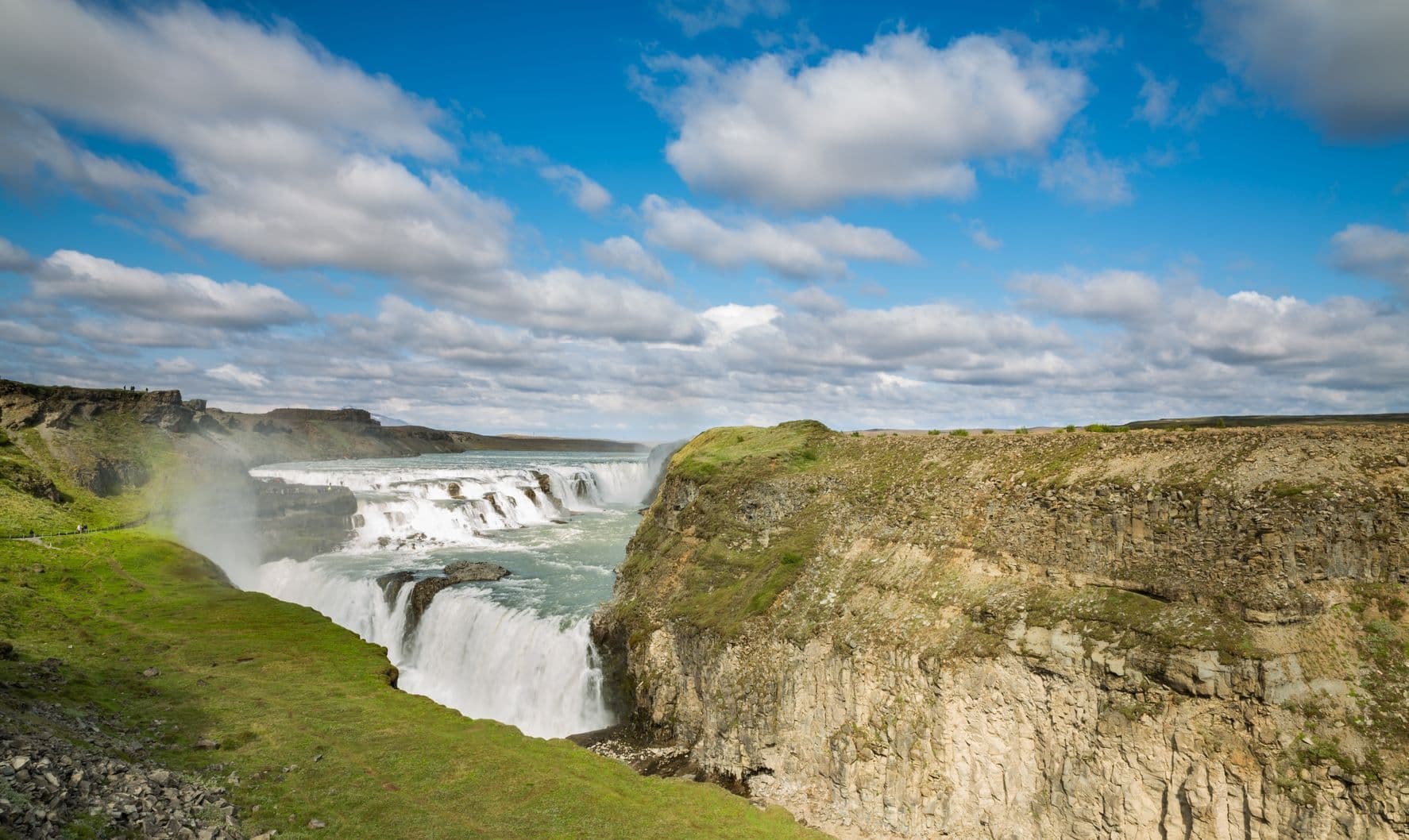 Gullfoss waterfall dropping in two tiers into its canyon, a faint rainbow in the spray
